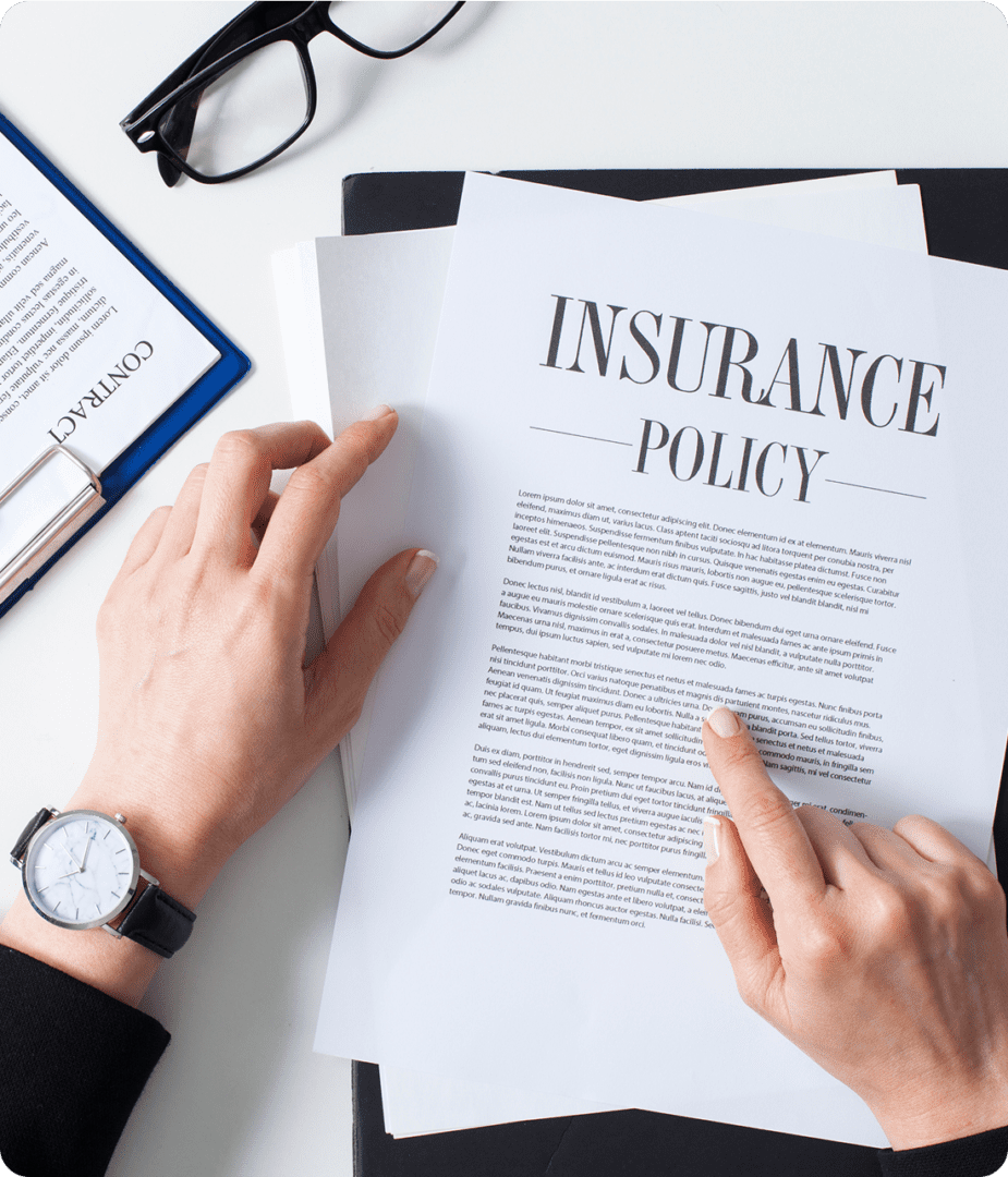 Hands holding an insurance policy document on a desk with a watch, glasses, and folders.